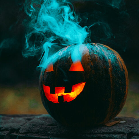 A vertical shot of an illuminated scary jack-o-lantern with green smoke